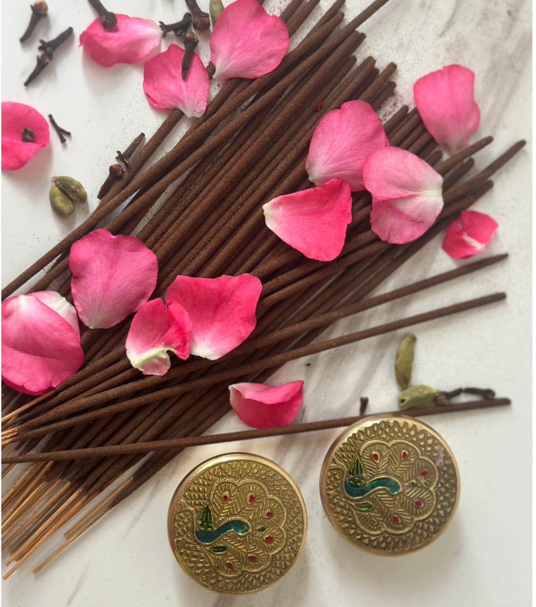 Incense sticks with pink petals and decorative gold buttons on a light background
