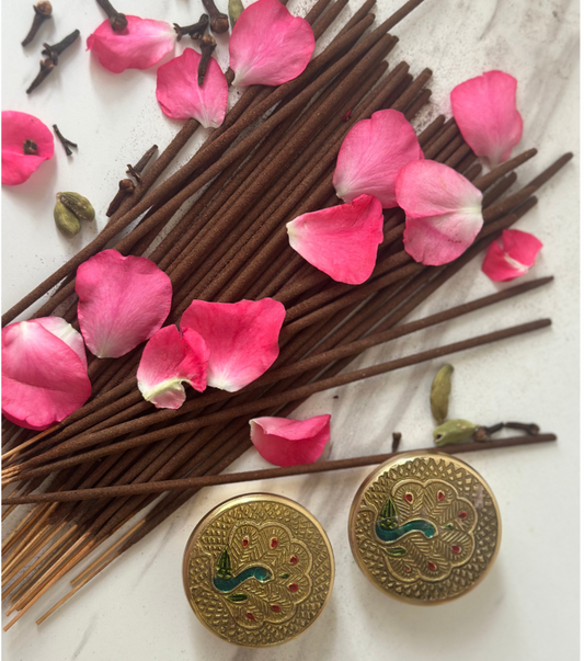 Incense sticks with pink petals and decorative gold buttons on a light background