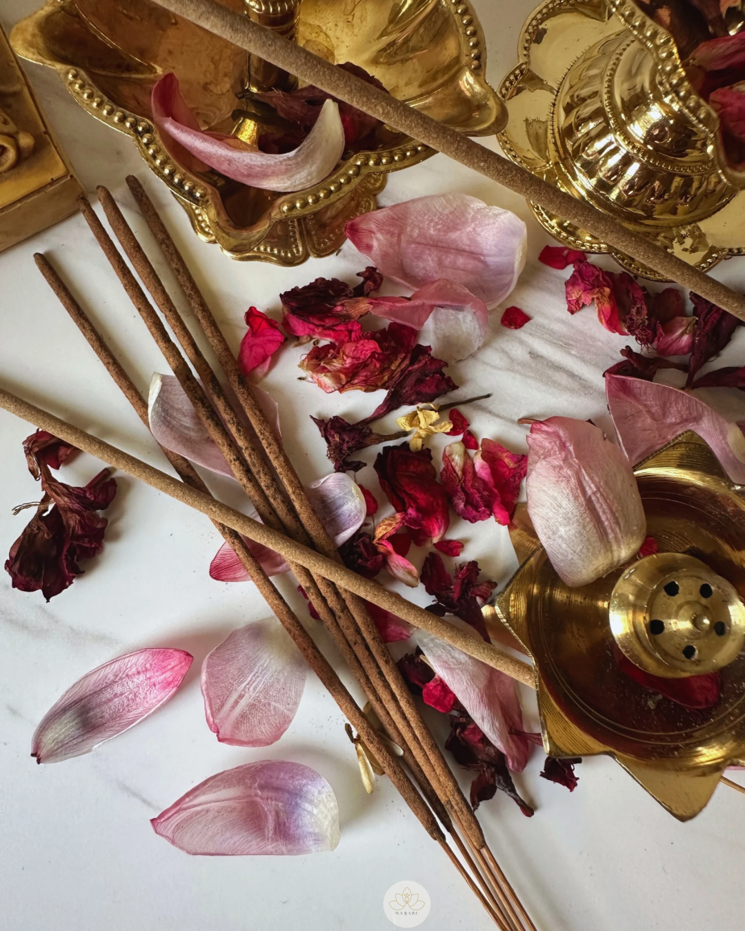 Incense sticks, rose petals, and a brass lamp on a white surface