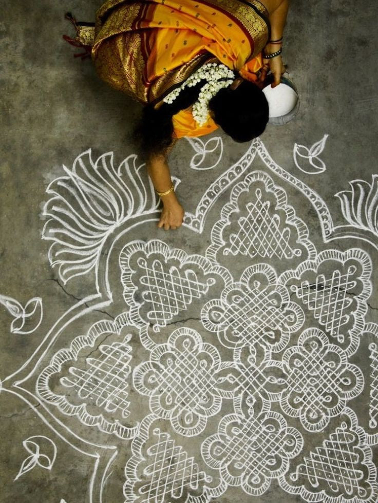 Woman drawing intricate white patterns on a gray floor with a container.
